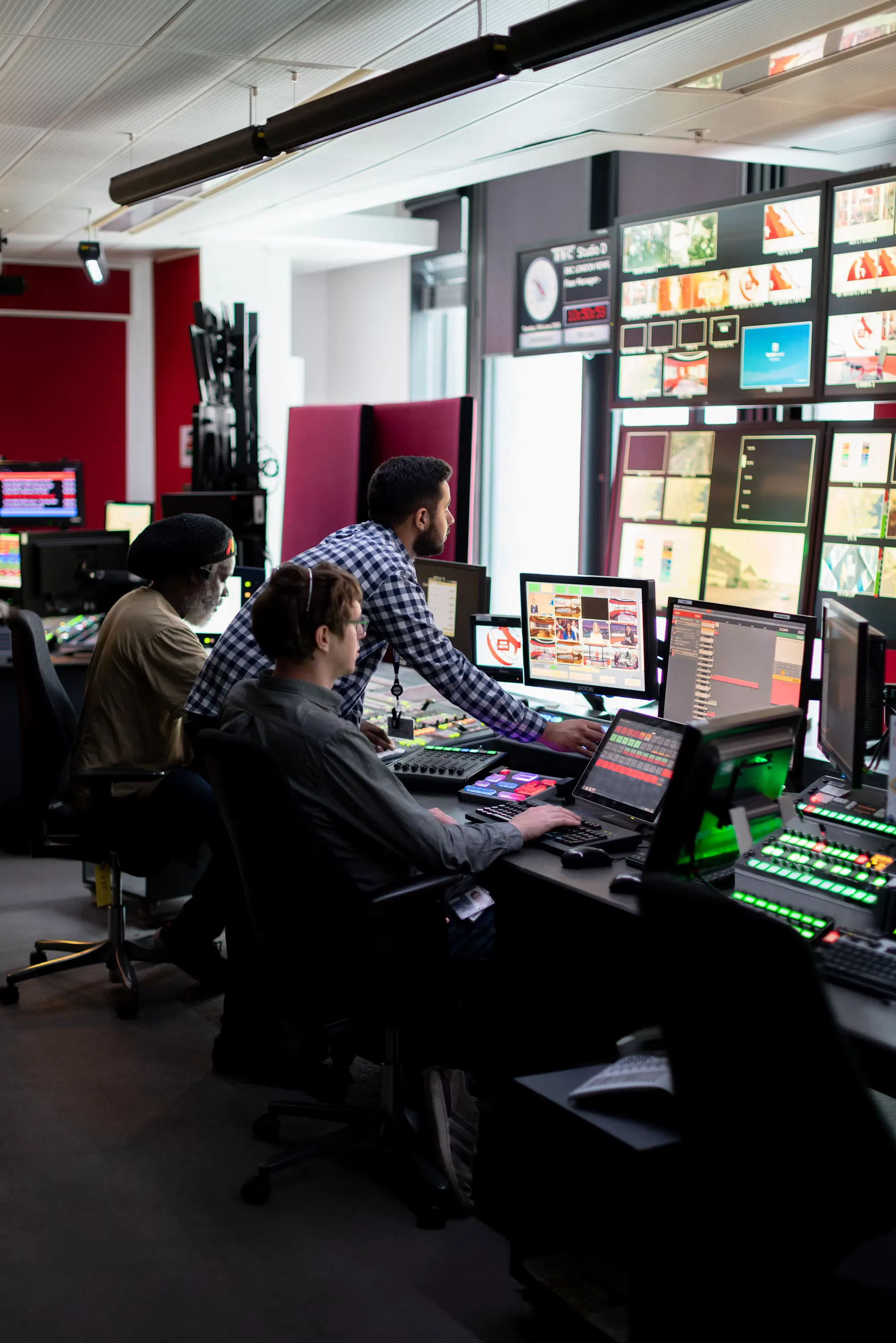 Three technical operators working side by side at a bank of monitors in a control room.
